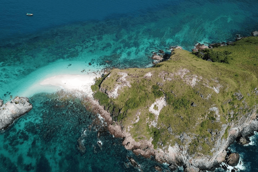 Aerial view of small green island, with sand flowing into crystal blue-green water.
